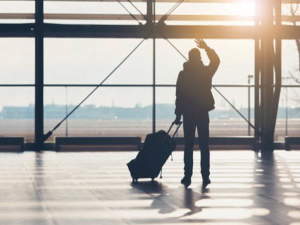 Man waving goodbye to friends and family at the airport while pulling luggage.